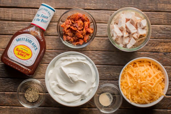 barbecue sauce, bacon, sour cream, cheese, and cooked chicken on a wooden table.