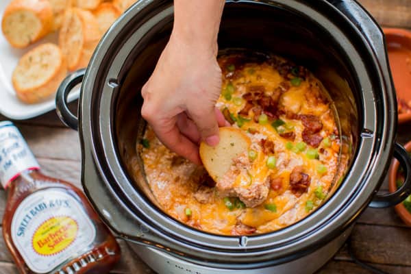slice of bread scooping barbecue chicken dip with Sweet Baby Ray's sauce.