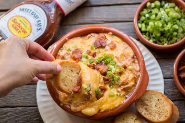 cheesy barbecue chicken dip in a bowl topped with bacon and green onion