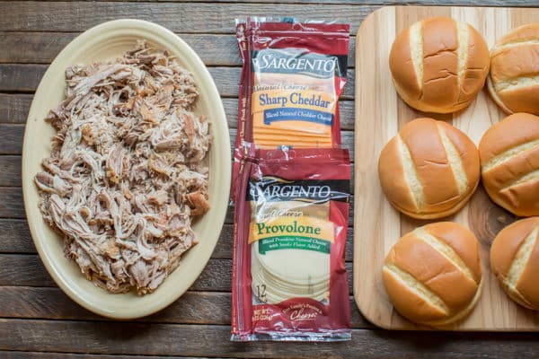 shredded pork, cheese, and buns on a cutting board.