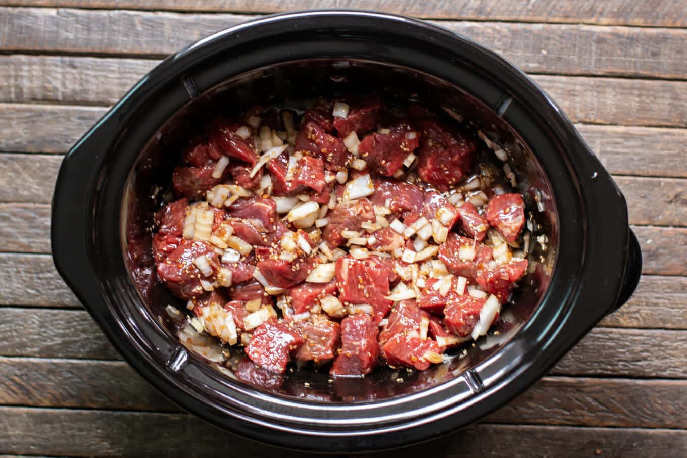 raw beef cubes with onion and teriyaki sauce in the slow cooker