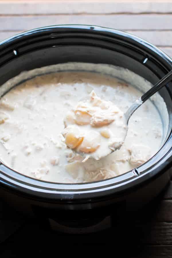 scoop of potato chicken soup coming from a slow cooker.