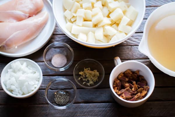 chicken breasts, potaotes, bacon, onion and seasonings on a wooden table.