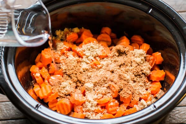 water being poured over carrots in a slow cooker.