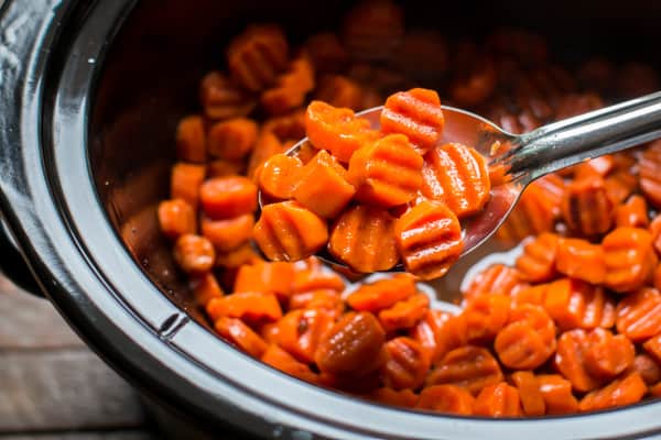 wavy sliced cooked candied carrots served from a metal spoon.