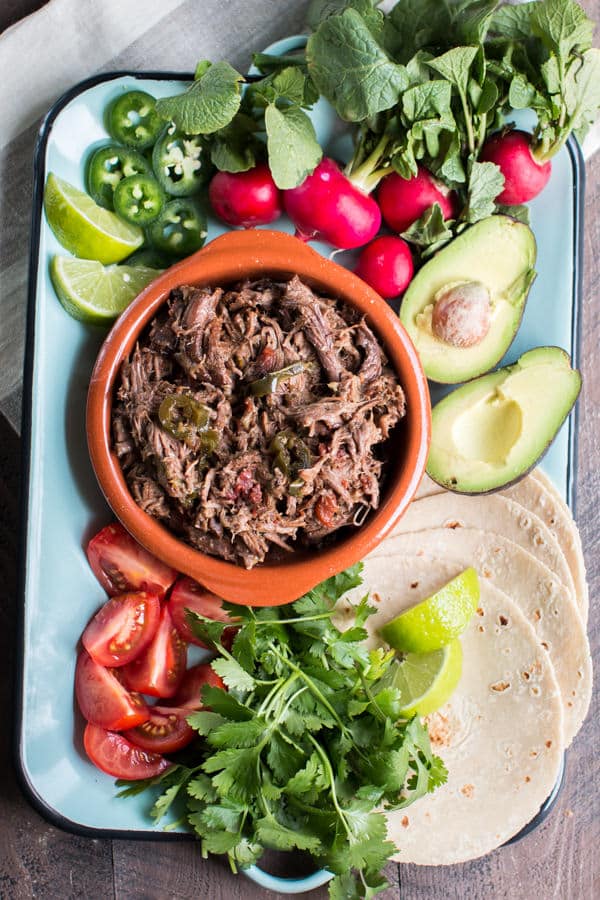 platter with avocado, radish, tortilla, onion, jalapeno, limes and shredded Mexican beef.
