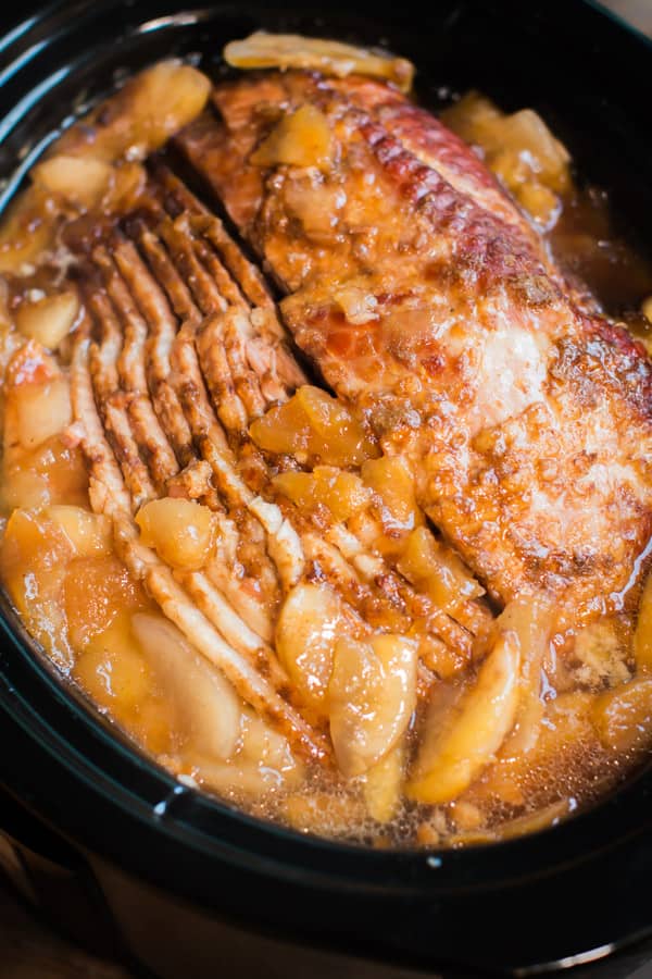 close up of spiral ham in the slow cooker with cloves and canned apple pie filling on top.