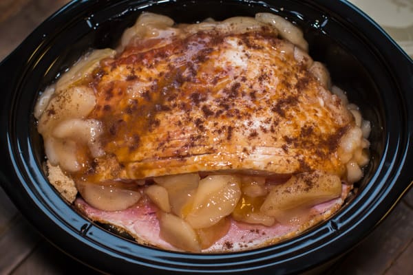 uncooked ham with sprinkled cloves on top. Apple pie filling around the edges of the ham.