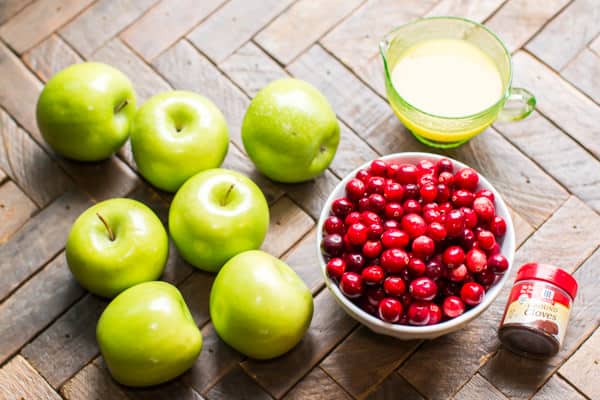 green apples, cranberries and orange juice on a wooden table.