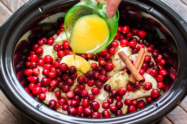 orange juice being poured over apples, cinnamon and cranberries.