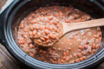 cooked pinto beans on a wooden ladle in  a slow cooker