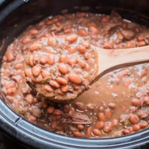 cooked pinto beans on a wooden ladle in  a slow cooker
