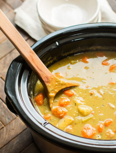 close up of split pea soup in a slow cooker with large wooden ladle in it.