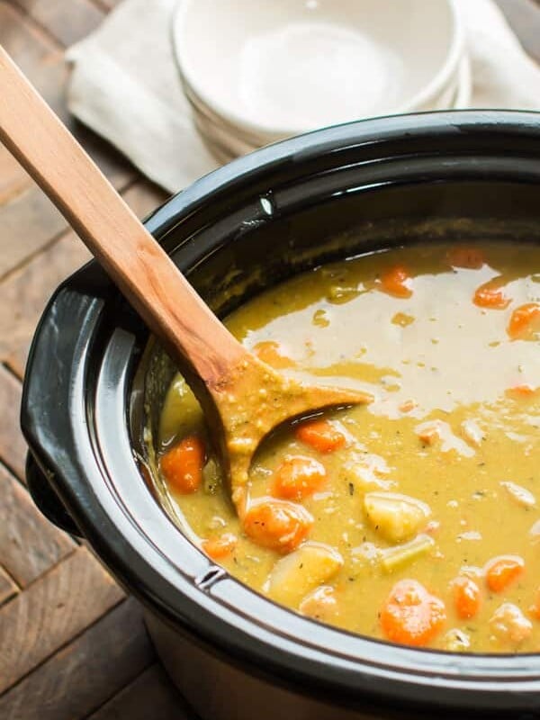 close up of split pea soup in a slow cooker with large wooden ladle in it.