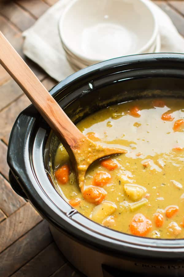 close up of split pea soup in a slow cooker with large wooden ladle in it.