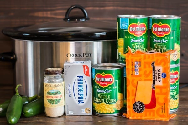 cans of corn, cheese, cream cheese, jalapenos, and onion powder in front of a slow cooker.