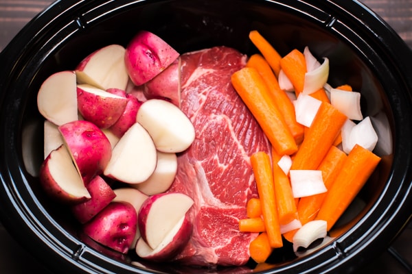 slow cooker with rase roast, carrots, and red potatoes.