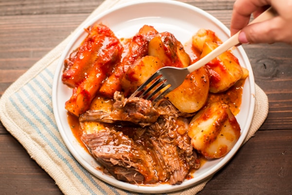 cooked pot roast with carrots and potatoes on a plate.