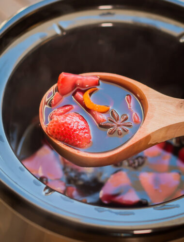 mulled wine in wooden spoon coming from slow cooker.