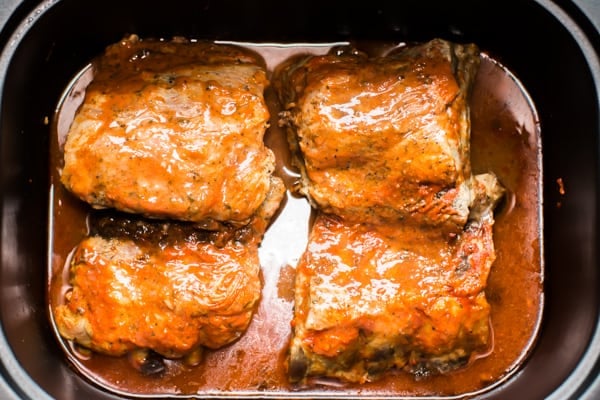 4 baby rack rib pieces with buffalo sauce in a slow cooker.