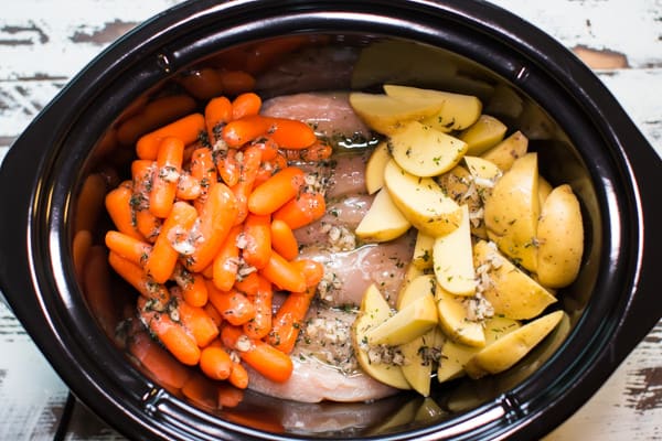 raw carrots, chicken and potatoes with garlic butter sauce uncooked in a slow cooker.