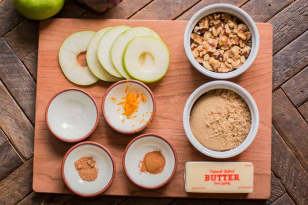 sliced apples, orange zest, brown sugar, butter, seasonings and walnuts on a cutting board.