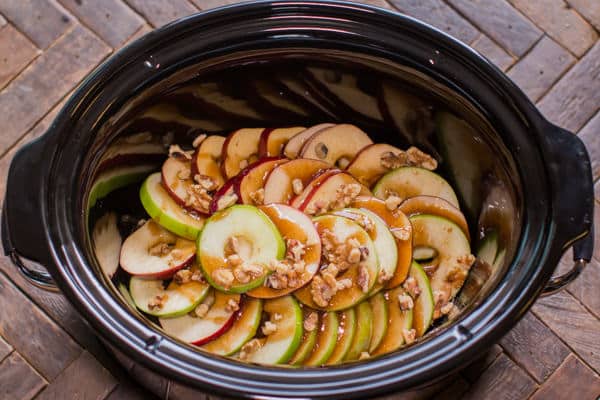 sliced apples in a slow cooker with glaze and walnuts on top.