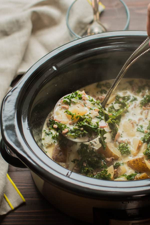 ladle of zuppa toscana soup coming from a slow cooker.