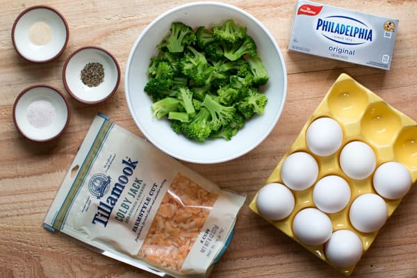 eggs, broccoli, cream cheese, colby jack cheese and pepper on wooden table.