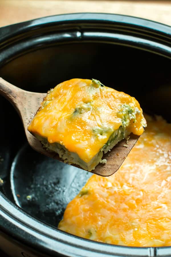 square or broccoli quice on a spatula. Slow Cooker in the background.