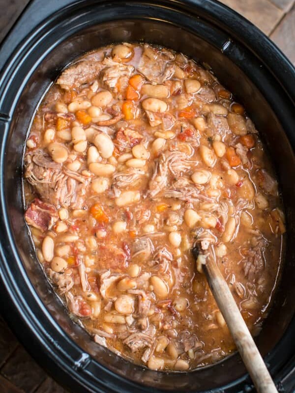 white beans and pork in a slow cooekr with a wooden spoon in it.