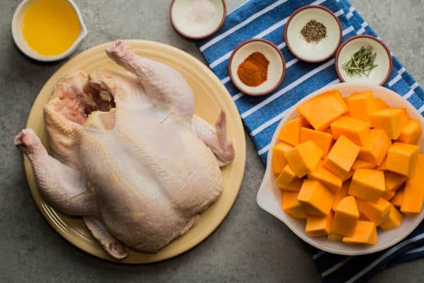 whole chicken, butternut squash, seasonings and melted butter on a table.