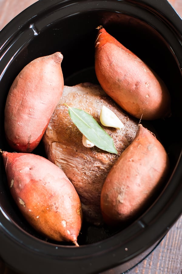 raw pork with sweet potatoes on top in a slow cooker.