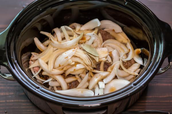 onions on top of a roast in a slow cooker.