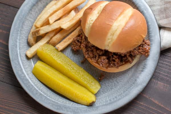 ground beef sandwiches with fries and pickles on a plate.