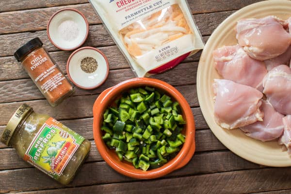 chicken thighs, pobalano peppers, green salsa, seasonings and cheese on a wooden table.