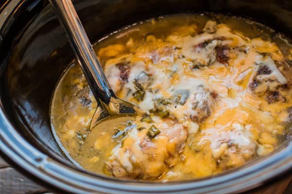 green chile cheesy chicken in the slow cooker with metal spoon in it.