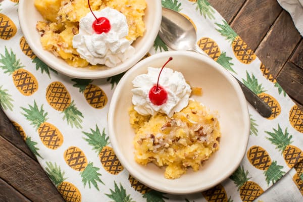 2 bowls of pineapple coconut cake with whipped cream and cherries on top.