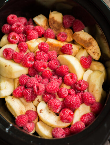 close up of sliced apples in a slow cooker with raspberries on top.