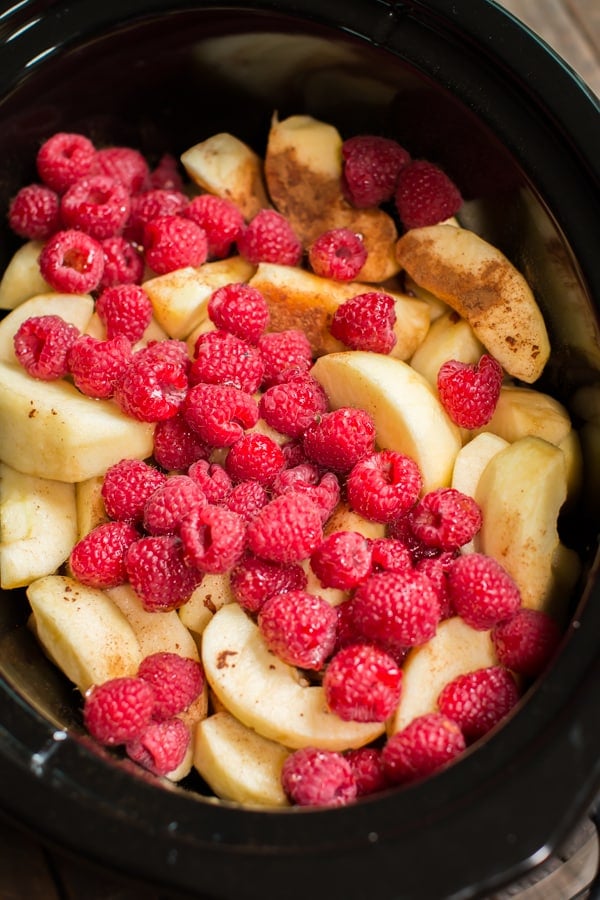 close up of sliced apples in a slow cooker with raspberries on top.