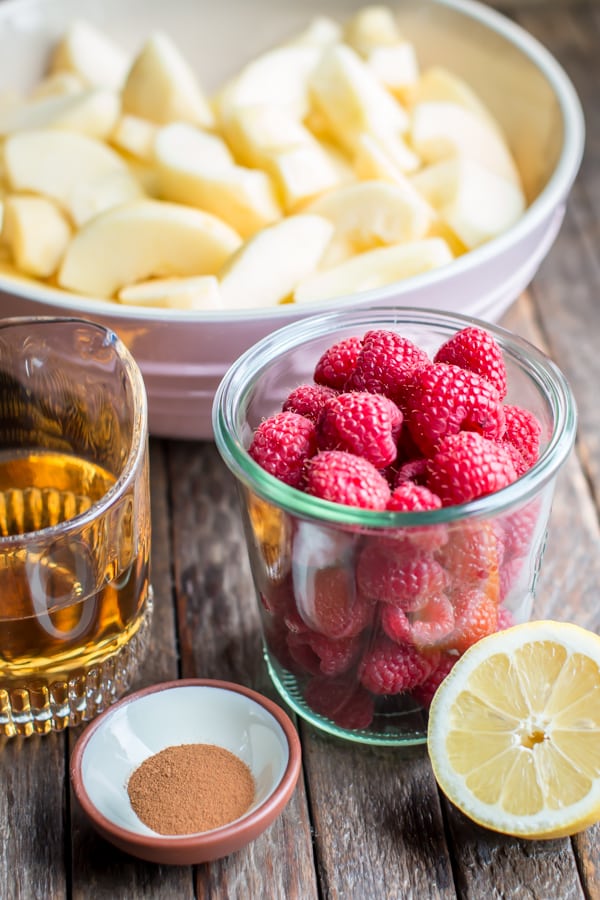 jar of raspberries, bowl of apples, lemon, cinnamon and apple juice on a table.