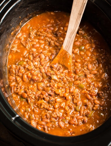 close up of baked beans with a wooden spoon in it.