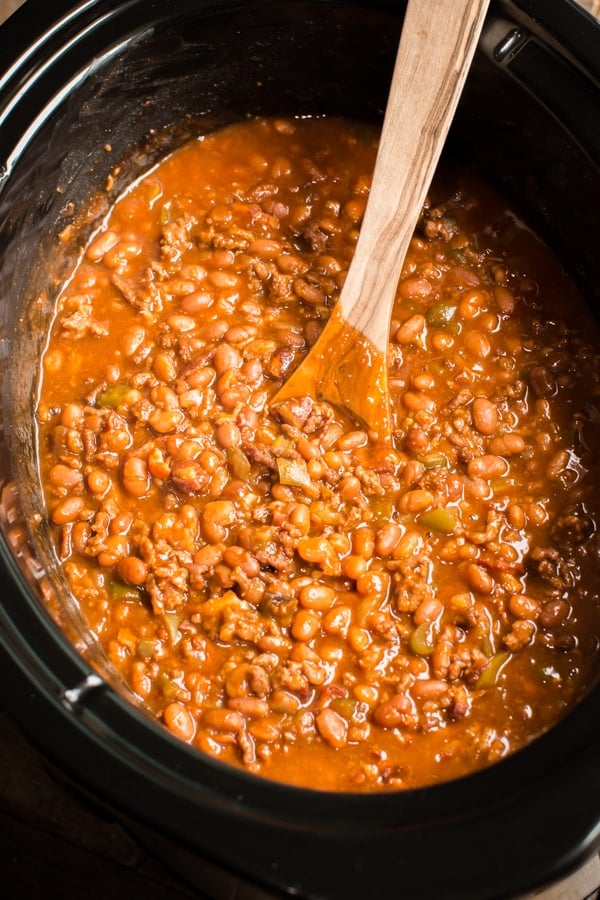 close up of baked beans with a wooden spoon in it.