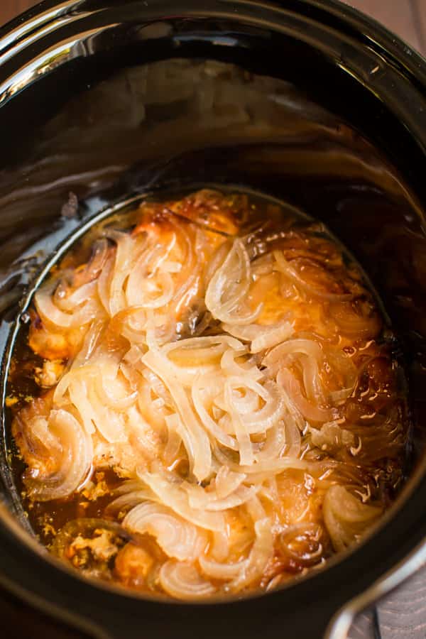 close up of pork chops in a slow cooker with onions.