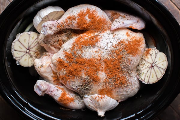raw whole chicken in a slow cooker with garlic. Paprika on top.