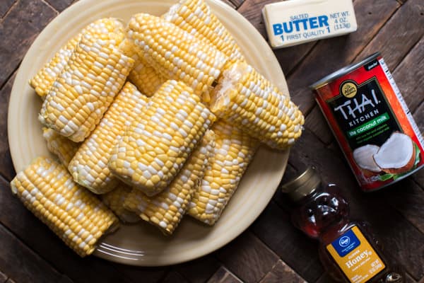 raw shucked corn on the cob, butter, coconut milk and honey on a wooden table.