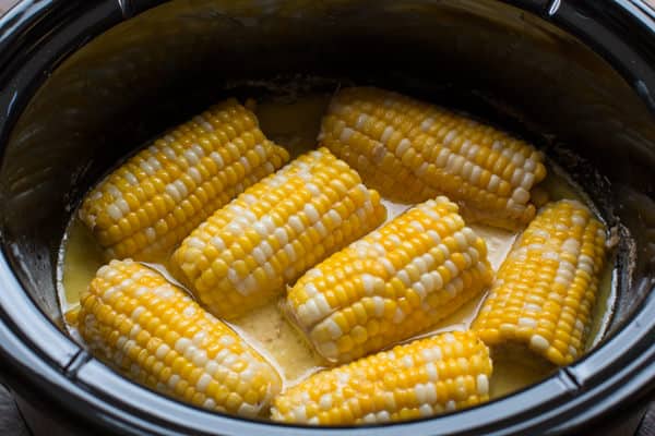 slow cooker with corn on the cob in a creamy liquid.