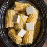 corn on the cob with pats of butter on top in a slow cooker.