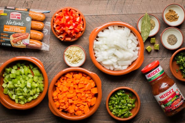 kielbasa, onion, carrots, celrey, peppers, bay leaf, salsa, garlic and seasonings on a wooden table.