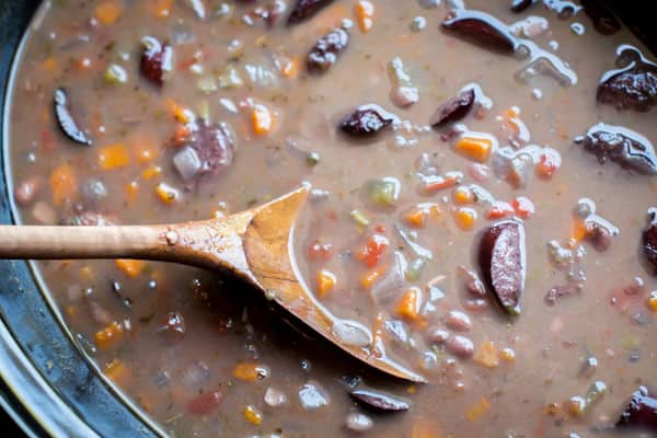 close up of kielbasa black beans soup with a wooden spoon in it.